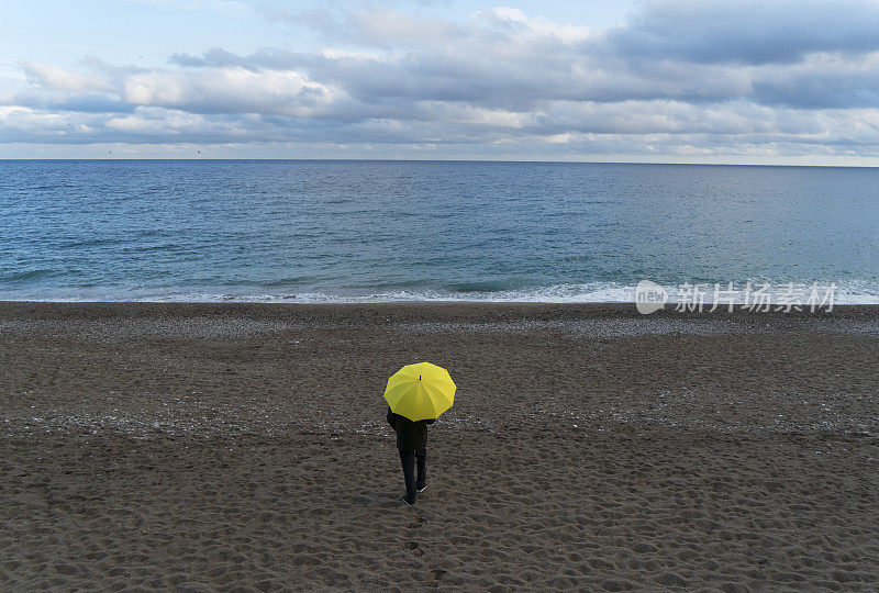 一个孤独的人在雨天走在海滩上