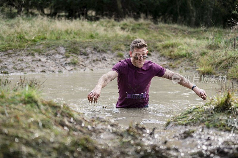 男子在齐腰深的泥泞溪流中参加户外慈善活动