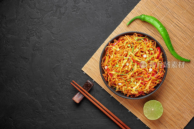 在黑色的石板桌面上，黑色碗里的中国贝勒。中国的巴勒是印中美食，以油炸客家面、蔬菜和四川酱为特色的街头小吃