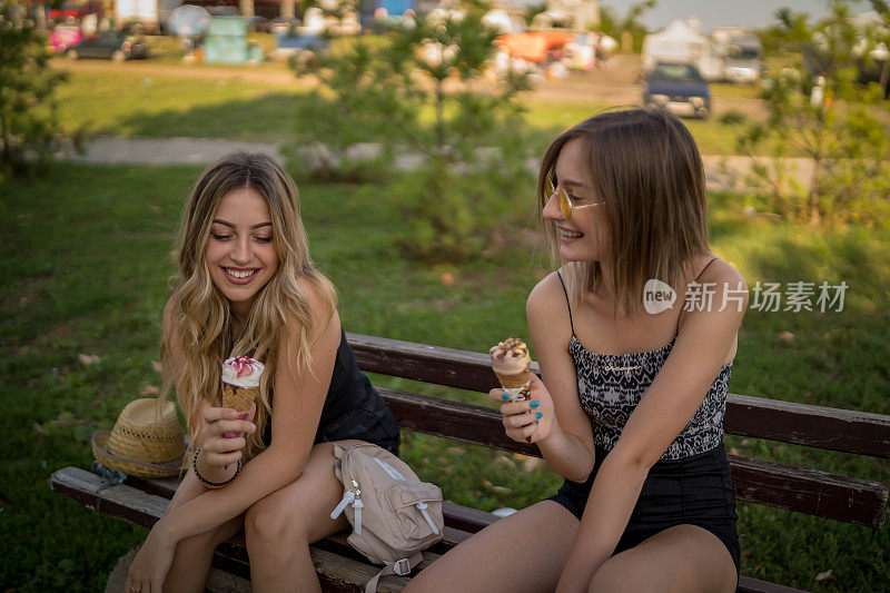 两个美丽的女孩在夏日公园散步，最后聊了起来。朋友们穿着时髦的衬衫和牛仔裤短裤，享受着休息日的乐趣。