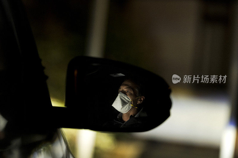 戴着面具的人在晚上开车时，侧面的镜子映出他的身影