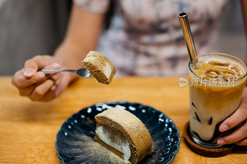 快乐的年轻亚洲女人享受瑞士卷和咖啡在咖啡馆