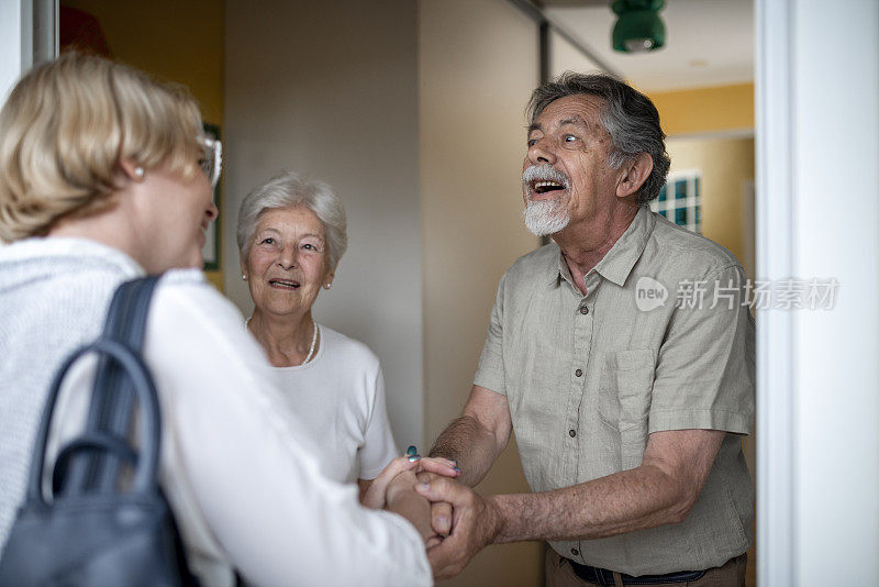 一对老年夫妇打开前门，迎接一名女性保健工作者进行家庭健康访问