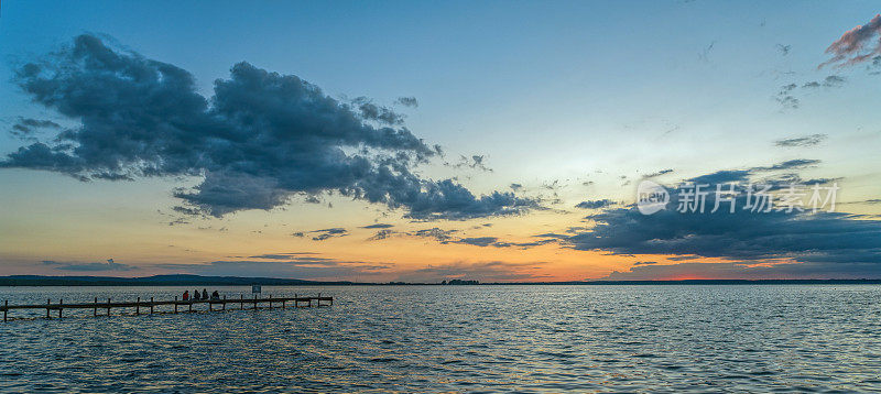 四人的剪影坐在湖边码头在黄昏与雄伟的云彩景观