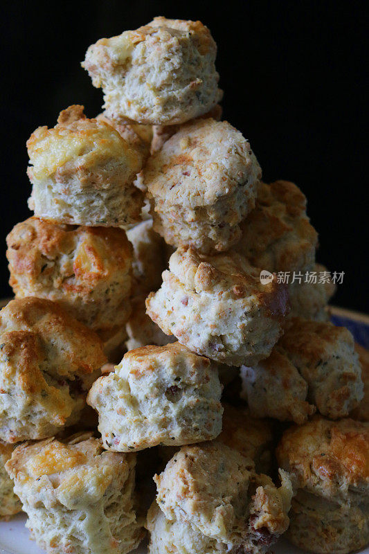 迷你自制奶酪烤饼堆在瓷盘上的特写图像，以黑色背景为背景，家庭烘焙的概念