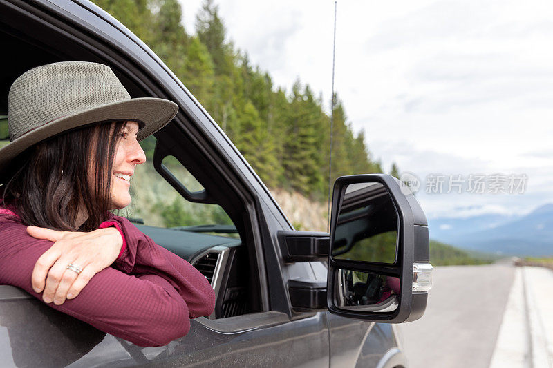 年轻时髦的女人靠在车窗上，一边开车一边欣赏风景