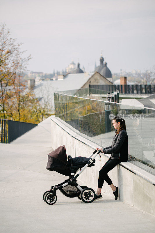 母亲推着婴儿车或婴儿车在现代城市的街道上散步和放松在秋天