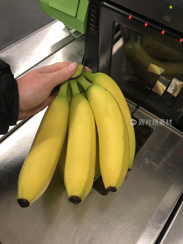 一个不知名的人拿着一串香蕉在超市自助结账处扫描(自助结账)