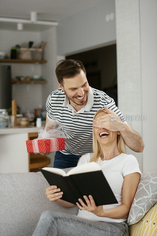 一个男人用礼物给他的女朋友一个惊喜。库存图片