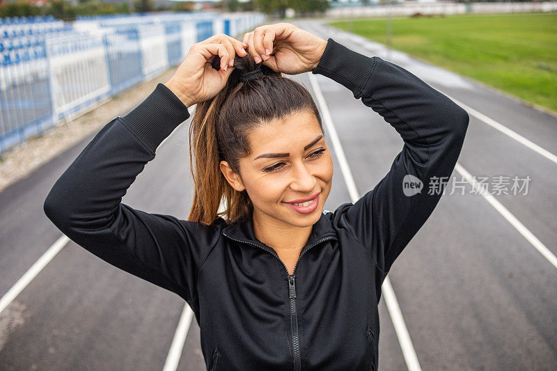 一个漂亮的健康的女人穿着黑色的运动器材在外面的跑道上锻炼。一个年轻漂亮的女人过着健康的生活。