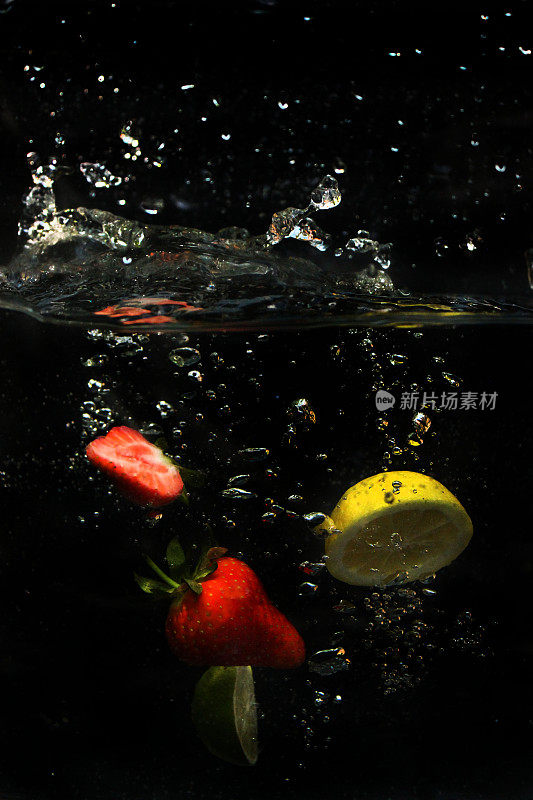 草莓、切片柠檬和酸橙水果落入水中，泡沫和飞溅的水珠在黑色背景下