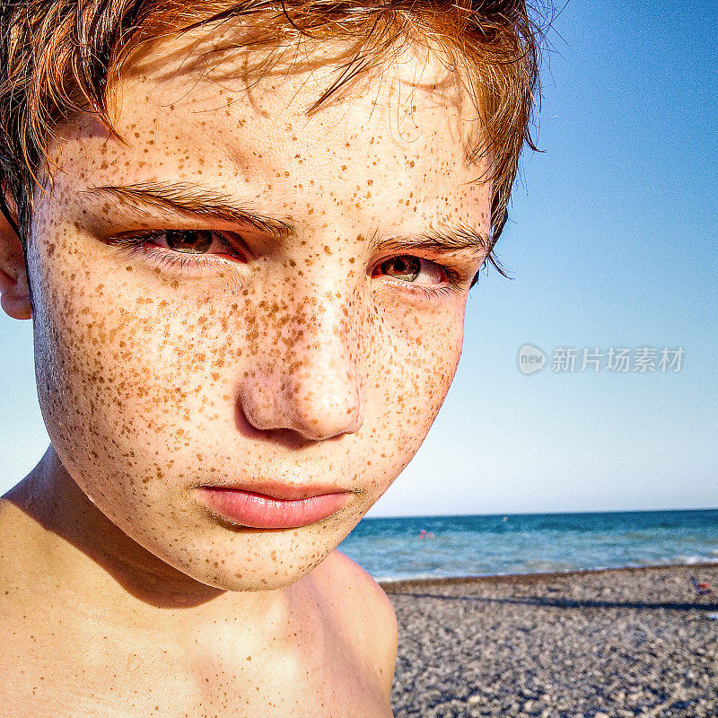 沙滩上长着雀斑的红发少年的肖像。近距离