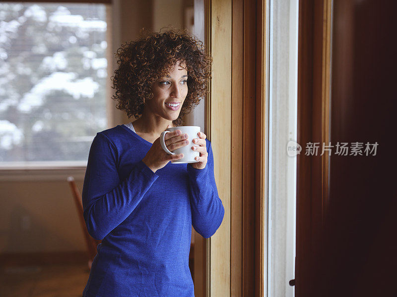 一个冬天站在窗前的家中的女人