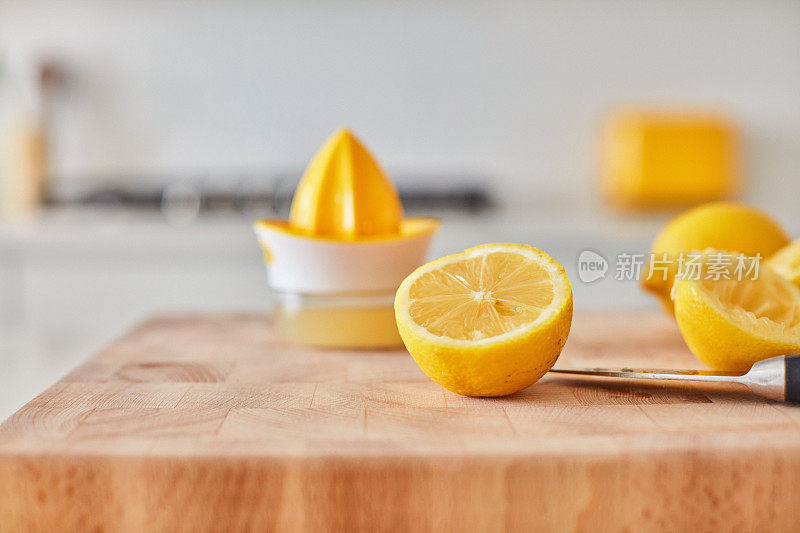 在明亮的现代厨房里，一个柠檬在砧板上的特写镜头。榨汁机，背景是柠檬汁。
