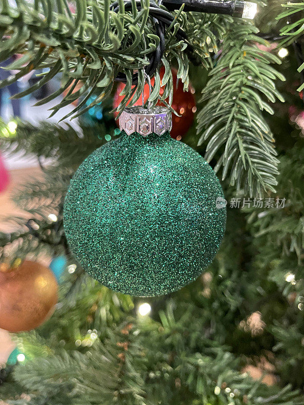 个人形象，绿色的闪光小饰物挂在人造圣诞树树枝，云杉针，模糊的白色精灵灯背景