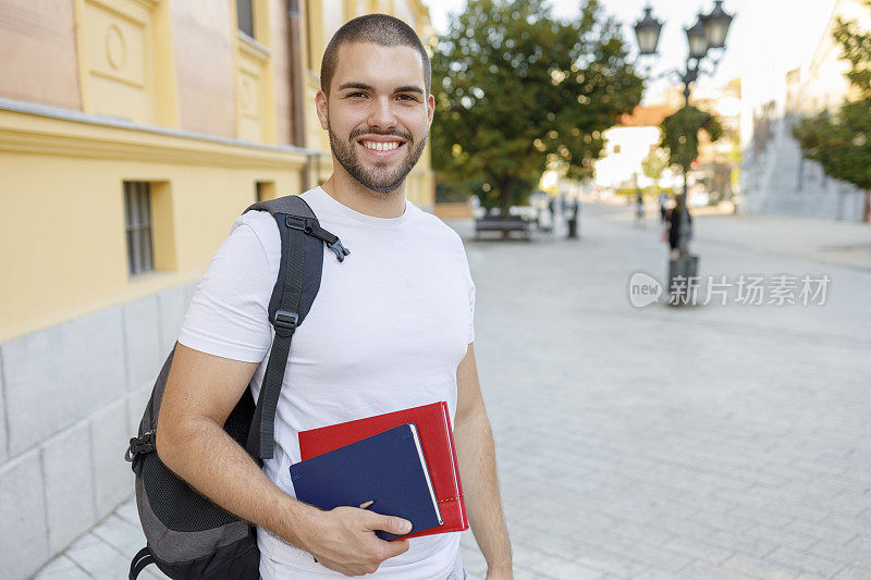 微笑的男学生拿着书在户外