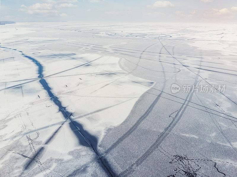 无人机俯视图的雪覆盖冻结的湖泊或河流表面与大裂冰对角线。自然冬季景观抽象纹理图案。在解冻季节，危险的池塘正在融化
