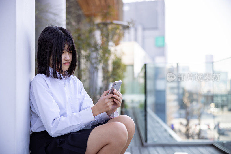 一个十几岁的女孩坐在屋顶上用智能手机