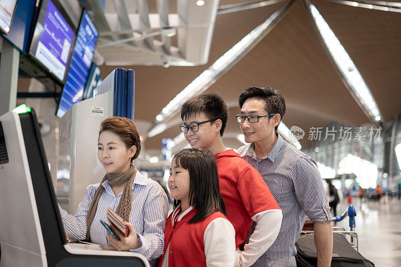 亚洲华人家庭在机场使用自动登机机办理登机手续。