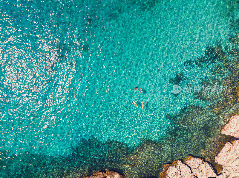 一个年轻的家庭在希腊岛美丽的海滩上漂浮和游泳的鸟瞰图