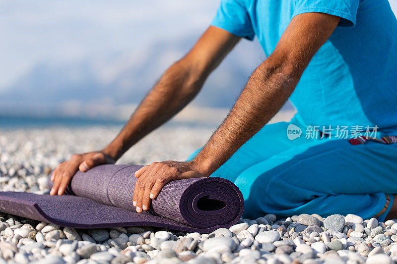 在日出或日落的时候，一个健康的年轻人在平静的海边做瑜伽练习前滚动垫子