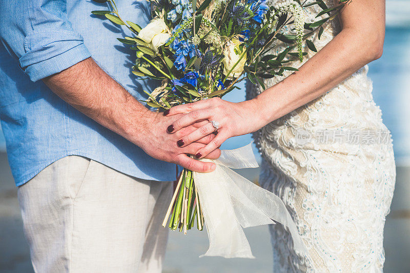 婚礼细节，新郎和新娘穿着结婚礼服，戴着钻石戒指，手持美丽的花束的特写