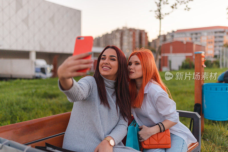 两个红发女子坐在户外公园长凳上自拍
