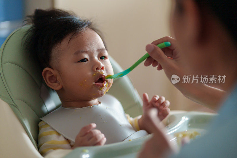 坐在高椅子上的亚洲小男孩正在被妈妈喂食。