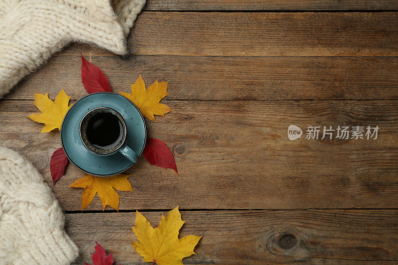 一杯热咖啡，毛衣和秋叶放在木桌上，平躺着。空间的文本