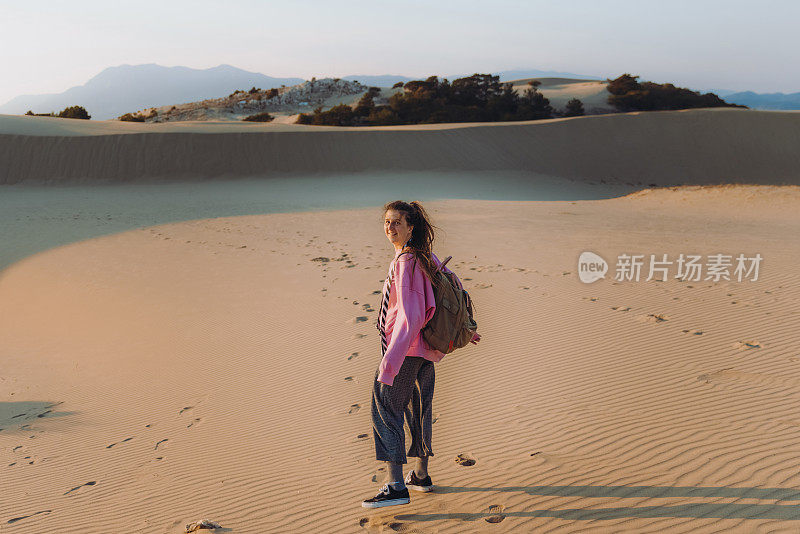 在土耳其海边的沙丘上，背着背包的女人凝视着风景优美的日落