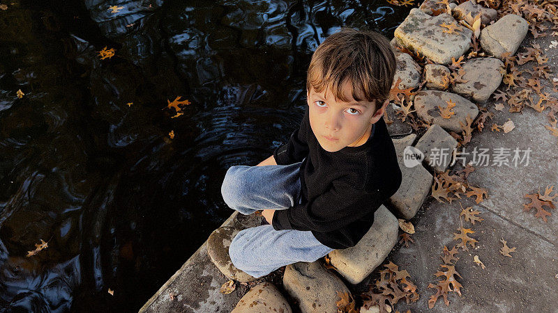 严肃的小男孩在池塘边玩水，看着相机