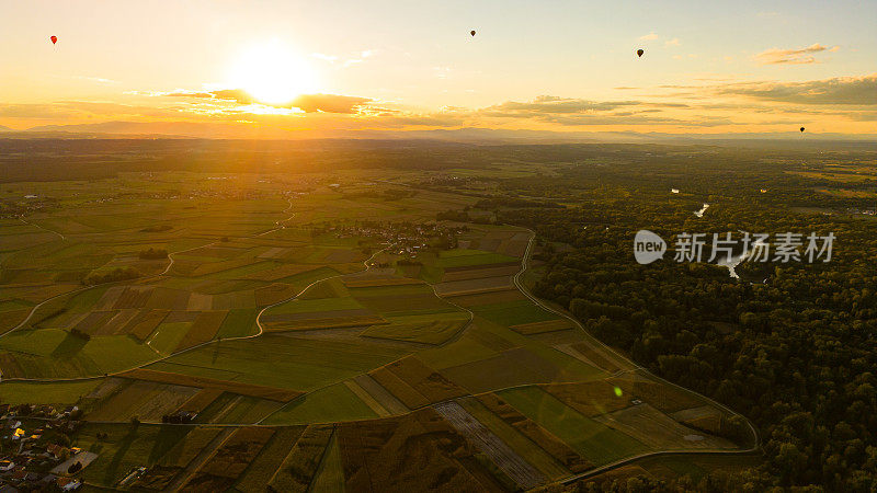 鸟瞰日出时，四个不同颜色的热气球在多个农田和森林上空翱翔