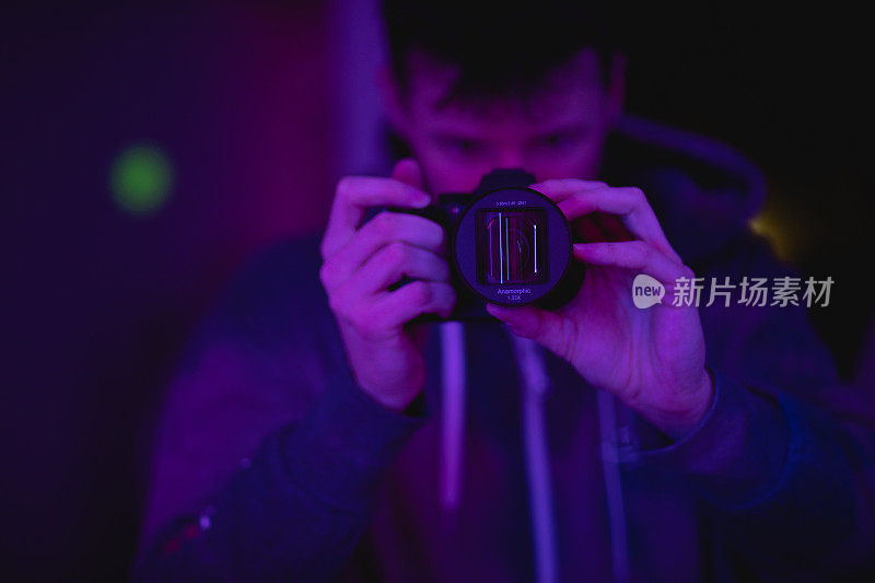 摄影师在室内霓虹灯色，人在专业相机设备上用变形镜头用紫色和粉色光拍摄。摄影师作为操作员，电影效果，生活方式概念摄影与选择性聚焦。