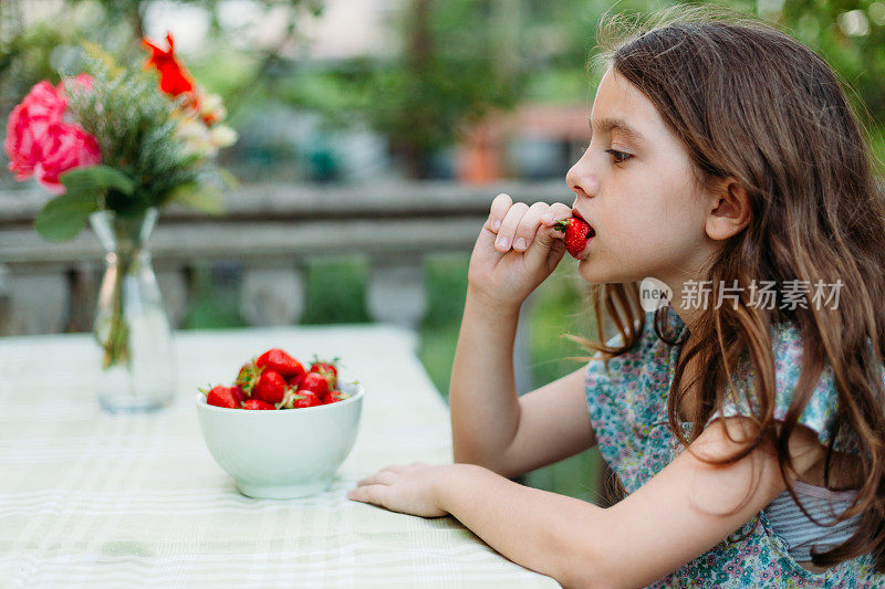 小女孩坐在桌边，吃着新鲜采摘的草莓