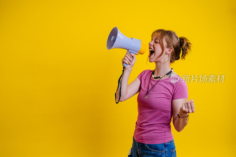 年轻女子在黄色背景下对着扩音器讲话