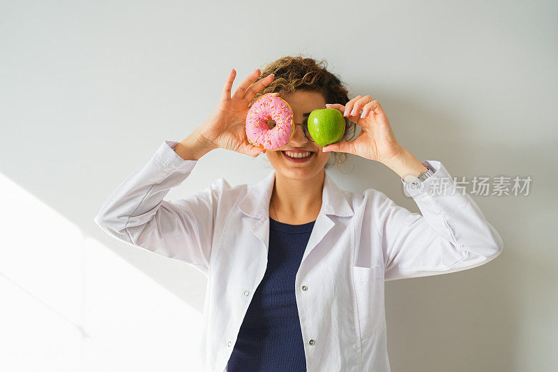 女性健康营养师用手捧着甜甜圈和苹果。健康饮食生活
