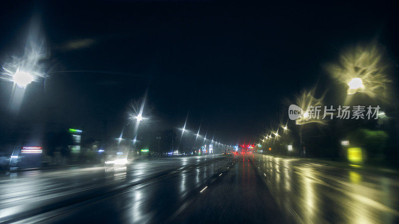 夜间在潮湿的照明道路上行驶:在暴风雨后的大雨中行驶。灯光模糊，轨迹散焦