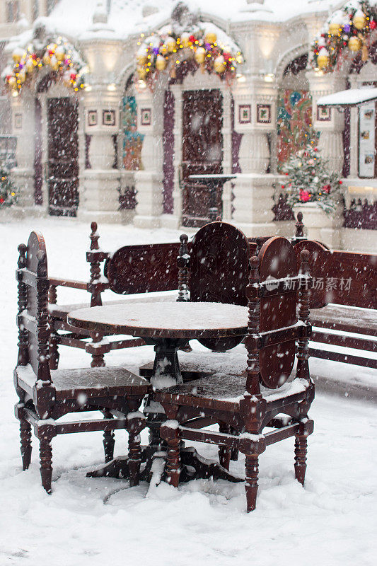一张木桌和几把椅子站在外面的雪下。冬天户外阳台上的咖啡桌