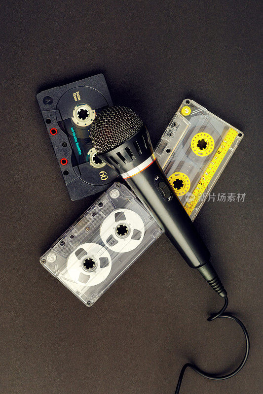 黑色专业卡拉ok麦克风和三个彩色复古录音带在黑色的背景。80年代模拟音频设备的垂直照片