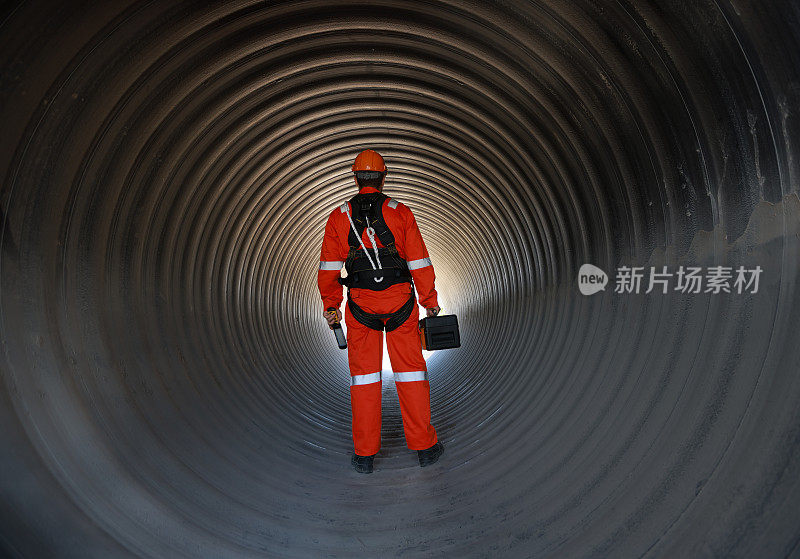 肖像工程师或技术人员穿着安全制服和安全带在施工现场的一个巨大的管道下工作。