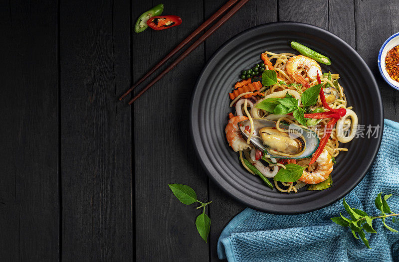 海鲜醉意面配虾鱿鱼蛤蜊辣椒和罗勒。泰国菜。黑色背景的桌子上，盘子里装着健康的亚洲人。前视图。