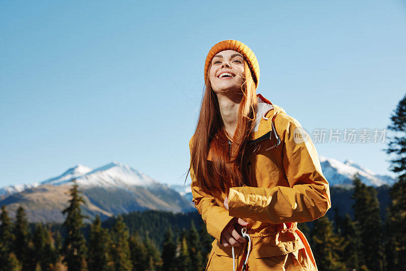 女人笑着笑着幸福和笑声旅游者穿着黄色的雨衣，红着头发在秋天旅行，在日落的阳光下在山上徒步旅行自由