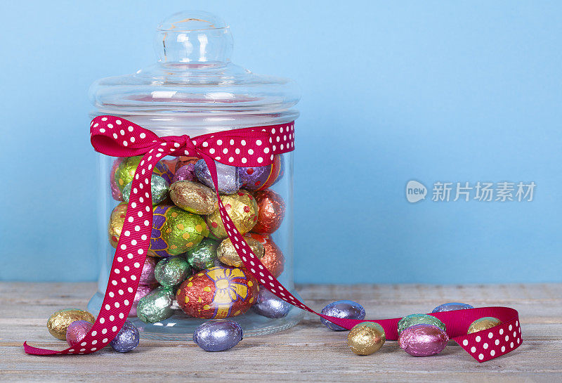 彩色巧克力复活节彩蛋在玻璃罐中，白色质朴的木桌。
