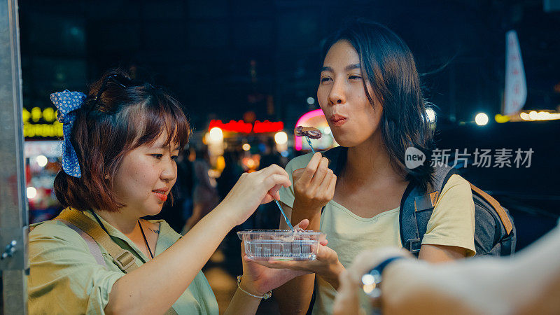 年轻的亚洲女性朋友背包客在泰国曼谷夜市的街头享受街头小吃。假日度假旅行。