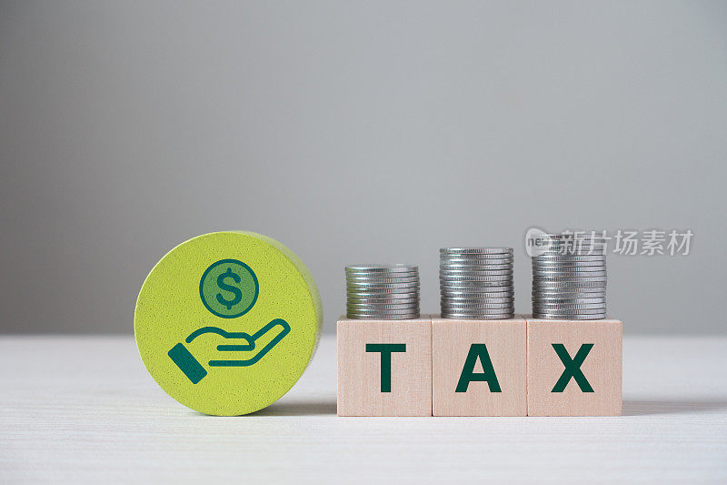 纳税概念。立方体与单词TAX和堆叠的硬币上的木制立方体块。税收抵扣规划、所得税申报、个人所得税、纳税、增值税、财产税、商务、金融。