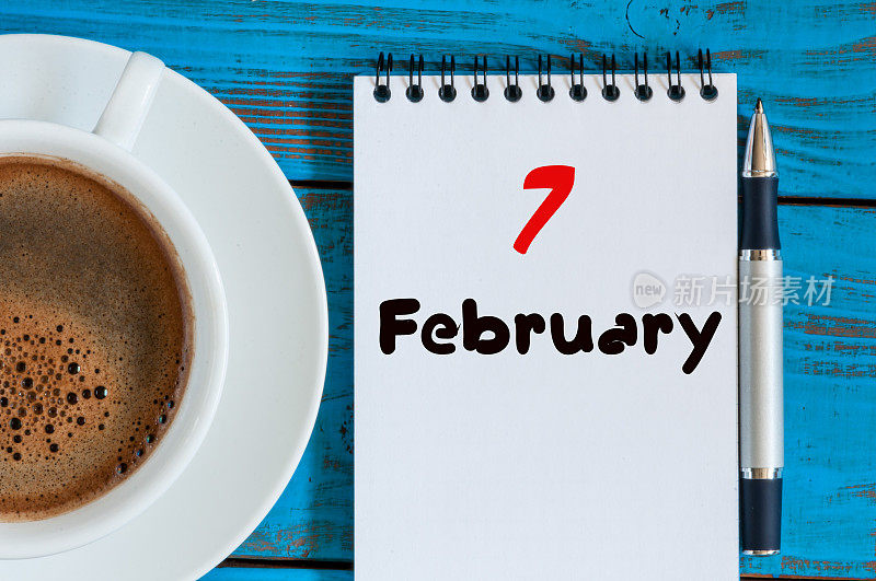 2月7日。月7日，日历在记事本上的木制背景上靠近早晨的杯子和咖啡。冬天的时间。文本空白