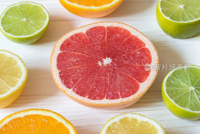 白色的木桌上放着几片柠檬、橙子、酸橙和葡萄柚。多汁的水果。模式的食物。宏。