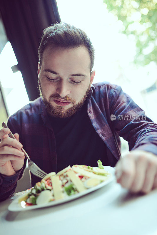 年轻的微笑的男人在早上吃新鲜的沙拉