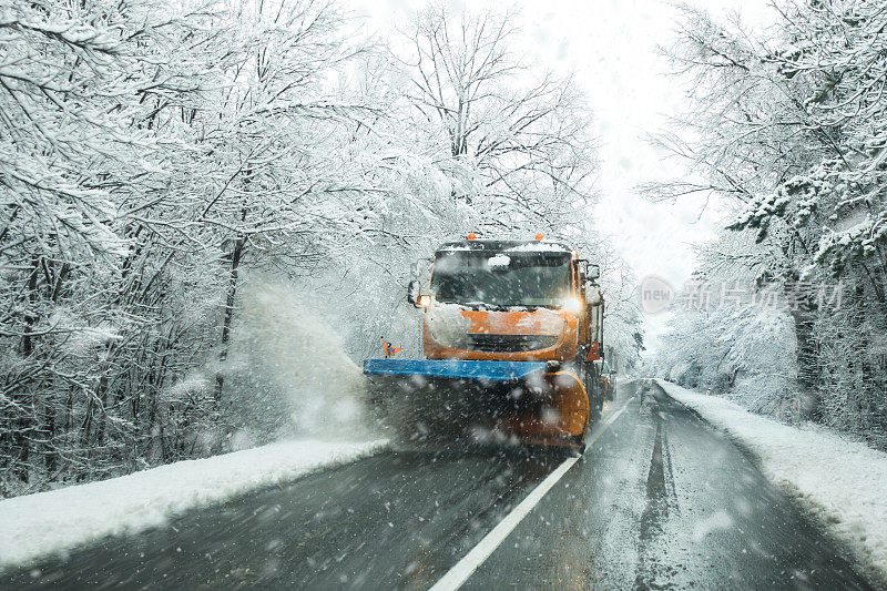 正面的扫雪机服务卡车和撒盐砂砾路面，以防止结冰在暴风雪的冬天的一天。