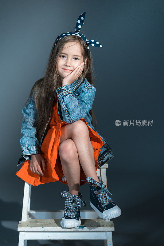 微笑的小女孩穿着牛仔裤夹克坐在台阶凳上